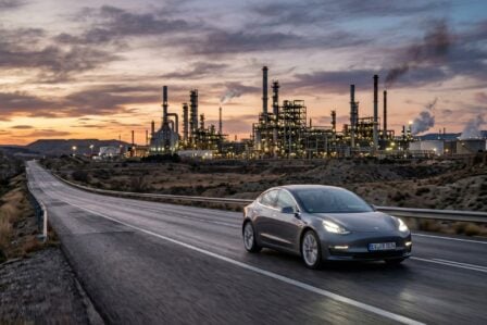 Voiture électrique sur route déserte avec raffinerie de pétrole en arrière-plan