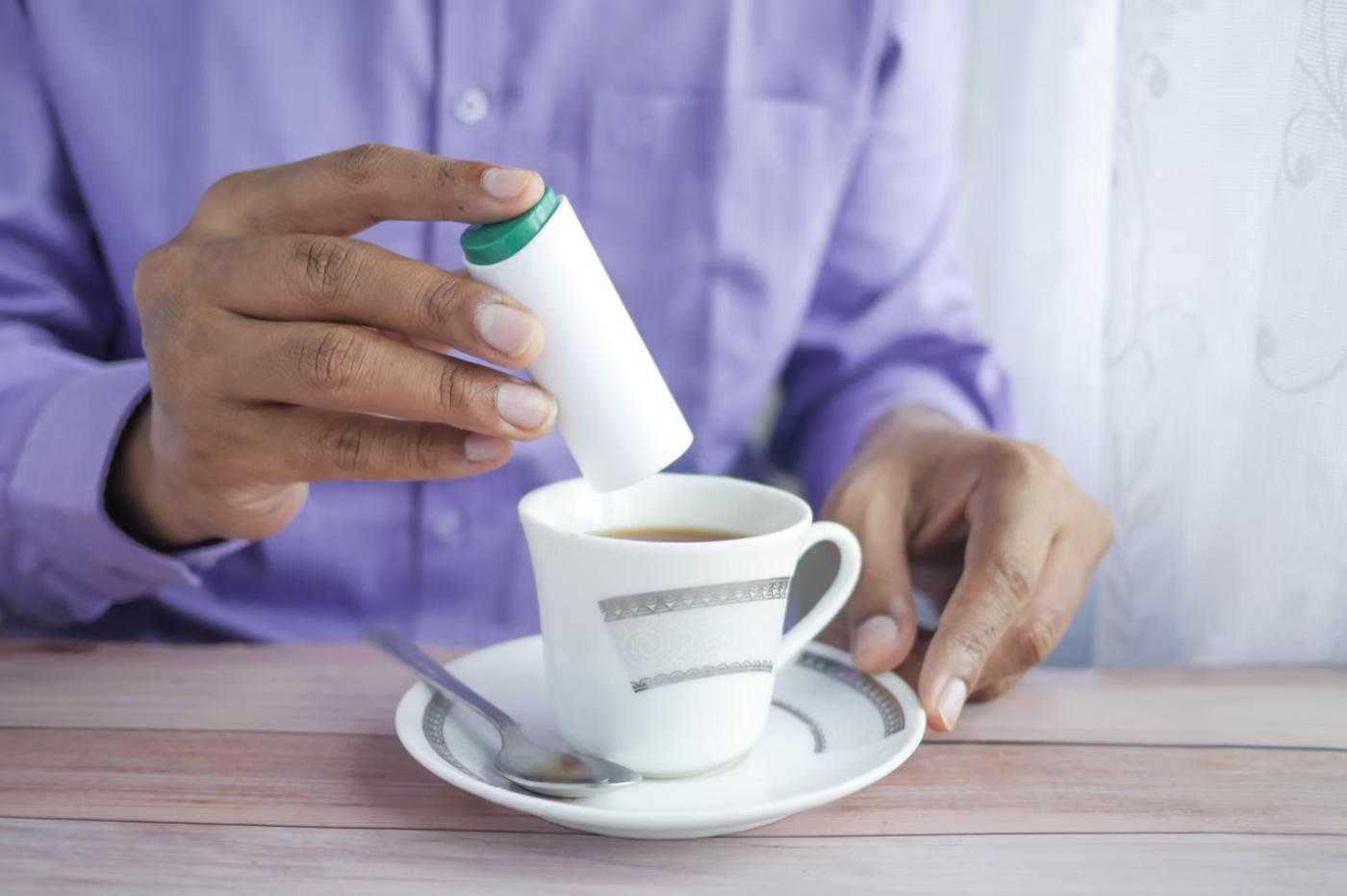 Une personne ajoute un édulcorant à son café.